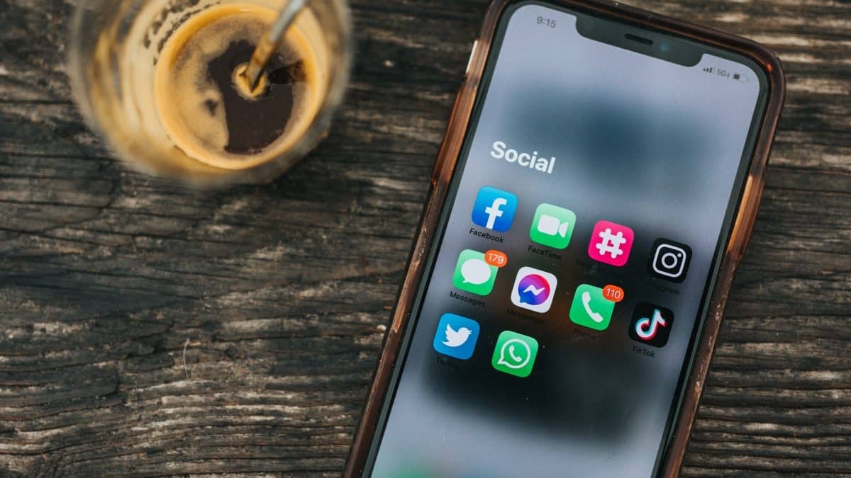 Phone showing social media apps on table next to drink